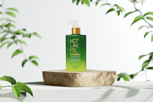 Green bottle of Sheer Glass Coat labeled 'Hot Like Me' on a wooden block with green leaves in the background
